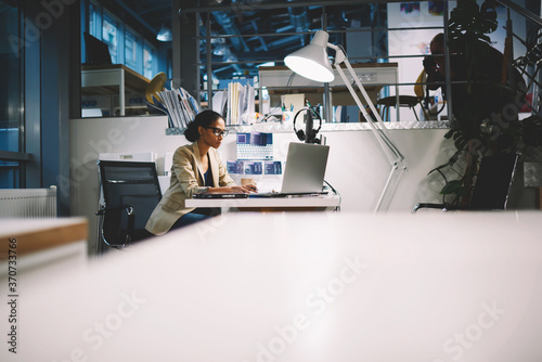 Busy female talented executive of trading company sitting in office on background having internet communication with customers monitoring sales via modern laptop computer connected to wireless network photo