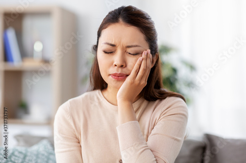 healthcare, dental health and problem concept - unhappy asian woman suffering from toothache at home photo