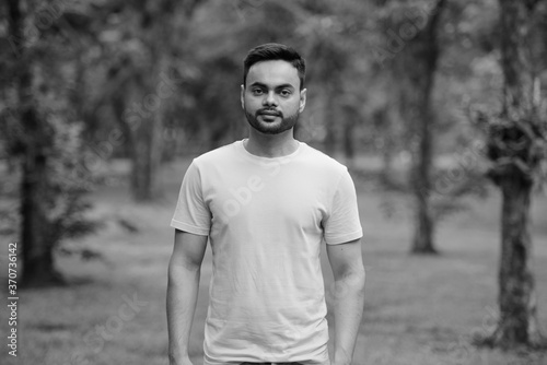 Young handsome bearded Indian man at the park in black and white