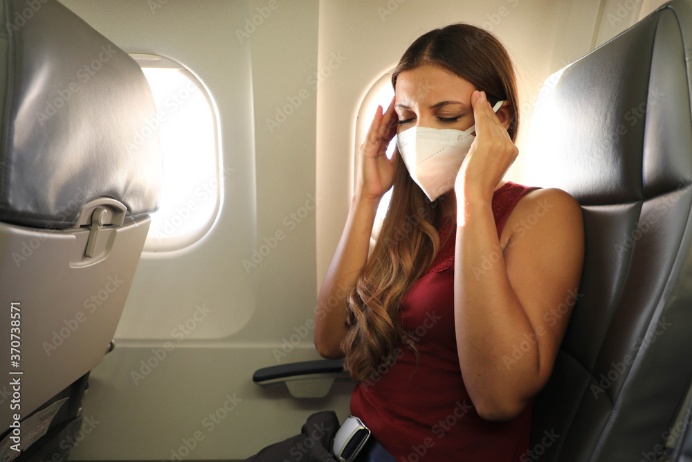 COVID-19 Young woman with KN95 FFP2 mask feeling unwell on plane. Fear of flying woman in airplane. Stress, headache, motion sickness and airsickness on plane during pandemic. - obrazy, fototapety, plakaty 