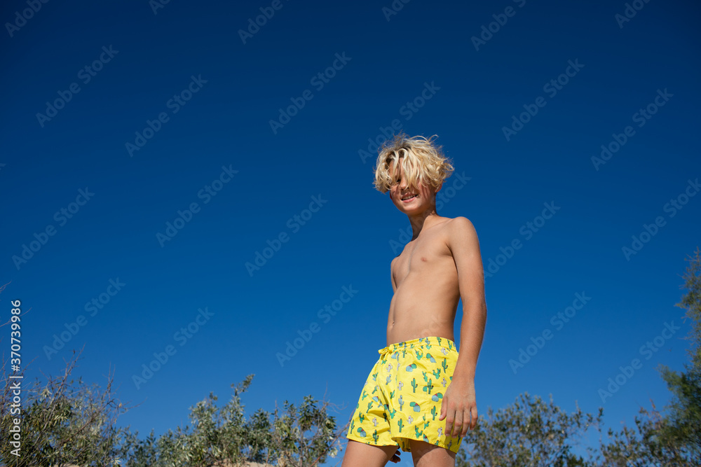 Young teen boy in yellow swim shorts posing on a sand hill at the
