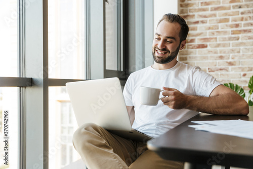 Image of man drinking coffee and using laptop while sitting at table