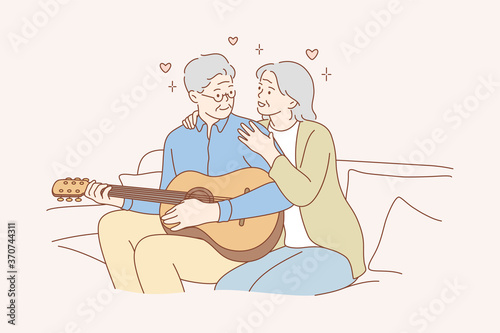 Couple, love, play, romance, music, recreation concept. Romantic old man and woman senior citizens pensioners sitting on couch together and playing guitar musical instrument at home. Happy retirement.