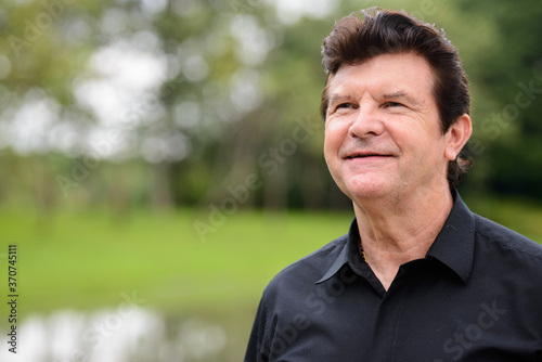 Portrait of happy mature handsome businessman relaxing at the park