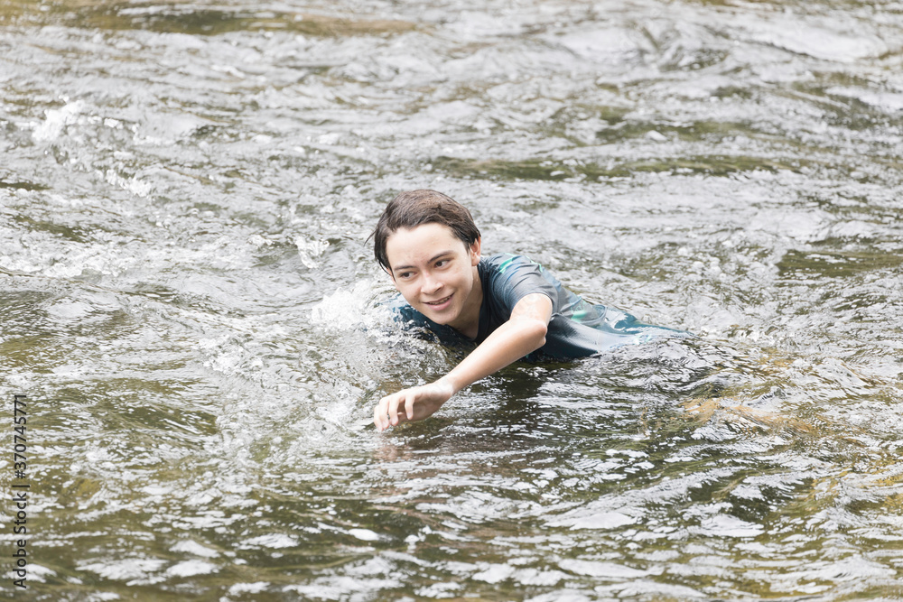 An elementary school boy was having fun playing in the fast flowing stream at Kiriwong village. Khiri Wong village is a famous village of natural tourism in Thailand.