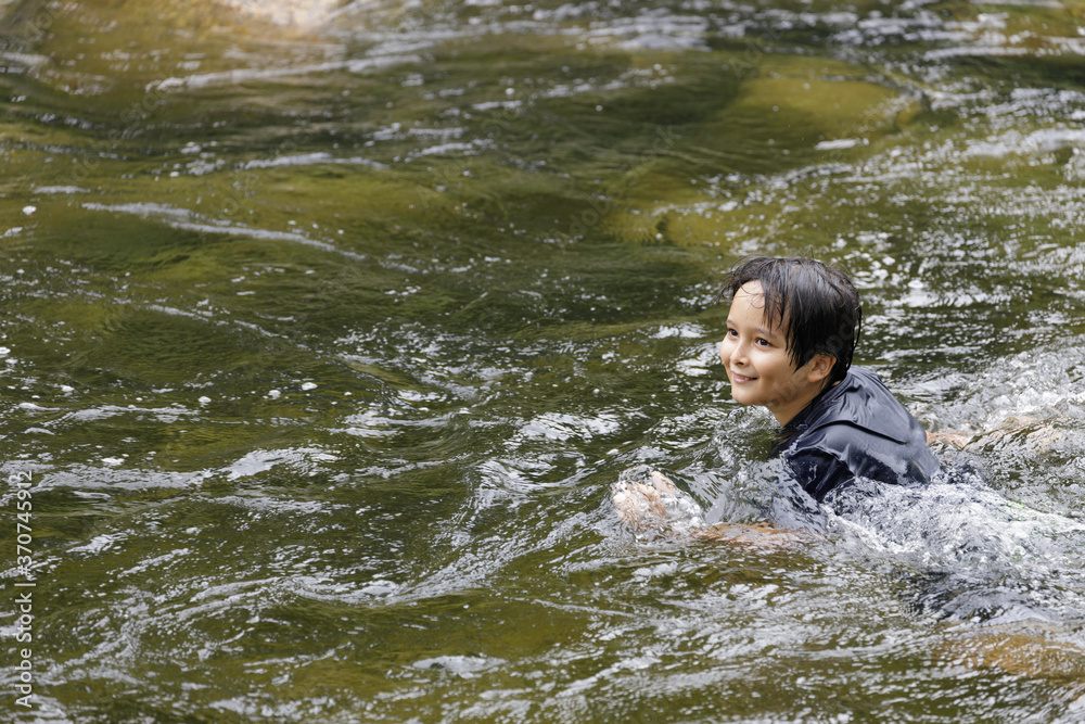 Obraz premium An elementary school boy was having fun playing in the fast flowing stream at Kiriwong village. Khiri Wong village is a famous village of natural tourism in Thailand.