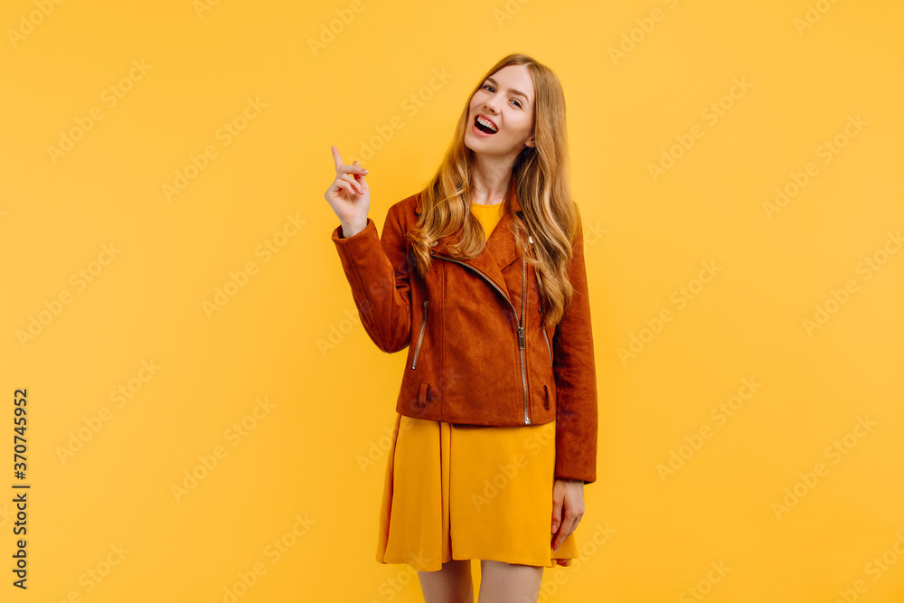 happy smiling beautiful girl, in a bright yellow dress and autumn jacket, points to an empty space to copy, has a positive smile, on an isolated yellow background. Autumn concept happy smiling beautiful girl, in a bright yellow dress and autumn jacket, points to an empty space to copy, has a positive smile, on an isolated yellow background. Autumn concept