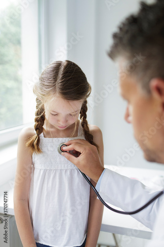 Doctor in white coat examines young, pretty girl in his practice or in a hospital