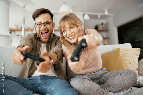 Husband and wife playing video game with joysticks in living room. Loving couple are playing video games at home.. photo