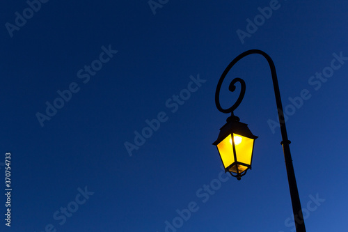 yellow light of night street city spiral metal shape lamppost on blue sky background 