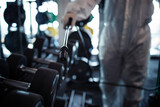 Close up view of gym disinfection and healthcare. Man in white protection suit disinfecting and fitness equipment and weights to stop spreading highly contagious coronavirus or COVID-19.