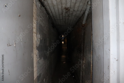 Isolated dark alley. Dim lighting at night. Eerie background in the dark. No people in image of alleyway between buildings. Old white and dirty walls. Ancient architecture needing refurbishment 