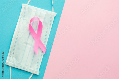Breast Cancer concept : Top view pink ribbon symbol of breast cancer campaign and and protective face mask on pink and bright blue