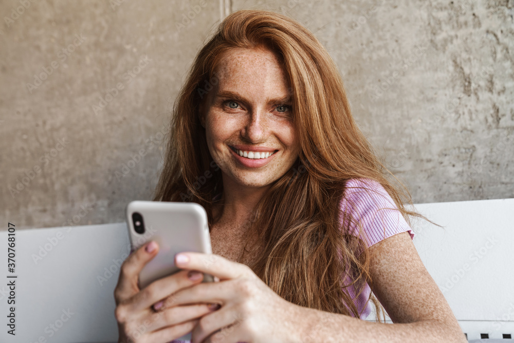 Image of woman smiling and using cellphone while sitting on couch Image of woman smiling and using cellphone while sitting on couch
