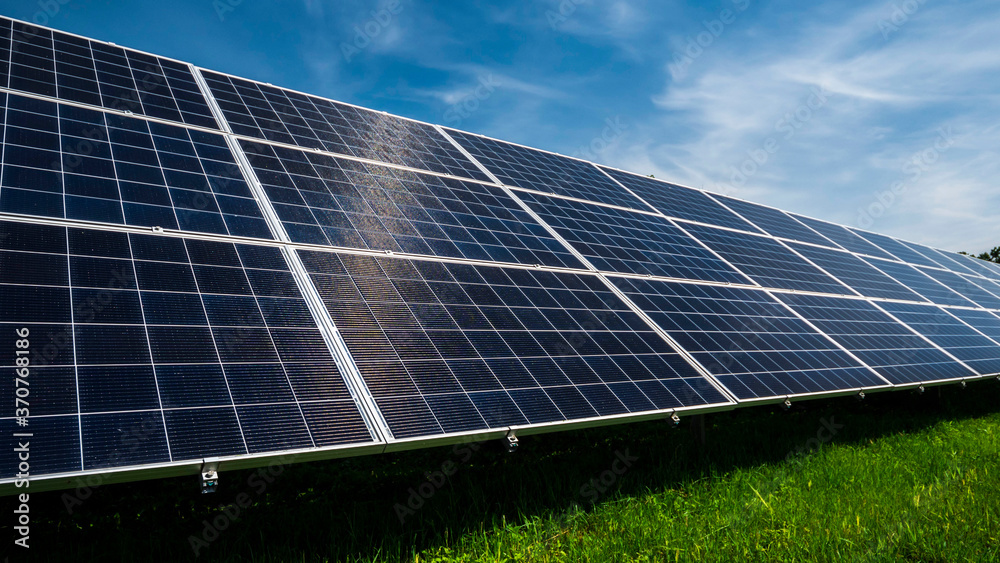 Solar power plant panels on a green meadow against a blue sky with clouds Solar power plant panels on a green meadow against a blue sky with clouds