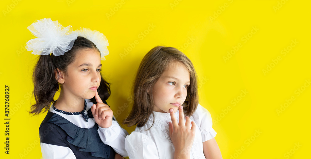 Two serious and dreamy schoolgirls. cute caucasian girls with brown and blond hair on yellow background. The concept back to school. Copy space Two serious and dreamy schoolgirls. cute caucasian girls with brown and blond hair on yellow background. The concept back to school. Copy space