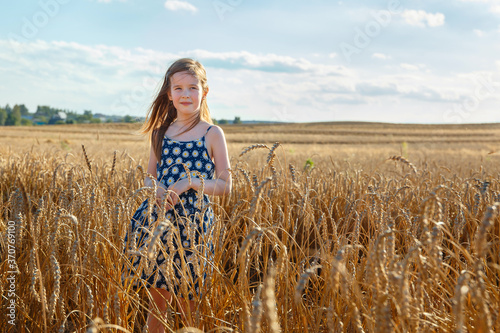 A little girl stands in a field in the middle of wheat ears