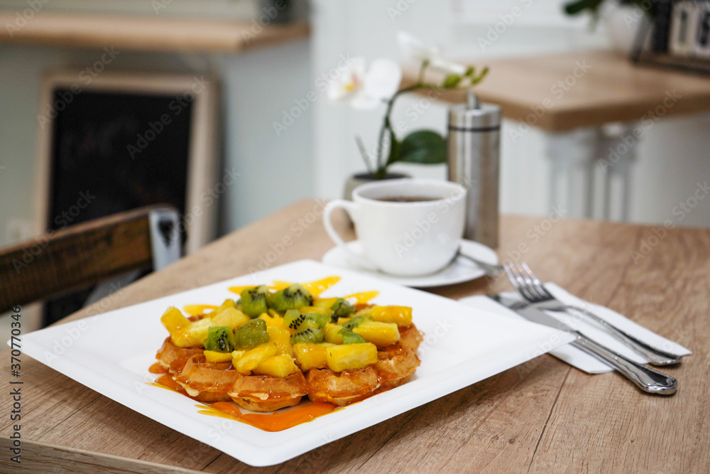 Delicious Viennese waffles with fruit and caramel in a plate on the table, Viennese breakfast over a mug of tea Delicious Viennese waffles with fruit and caramel in a plate on the table, Viennese breakfast over a mug of tea