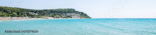 Blue sea and a beach in the background with green forest and small houses,at an area in Greece Chalkidiki