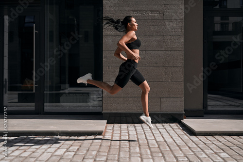 Young athletic woman running in the city, shot of girl jumps on the glass building background.