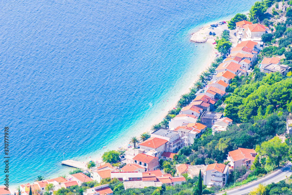 Aerial view down to the beach with blue water and white houses with orange roofs. Life in Croatia and holiday destinations. Background image.
