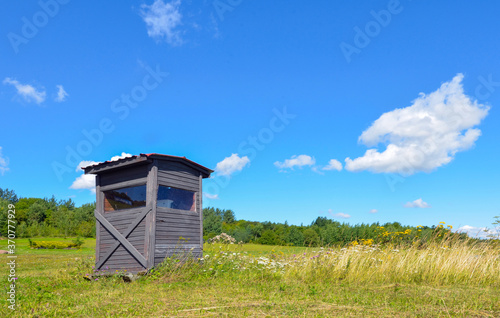 old wooden booth in green field and blue sky © Naira Chatilian