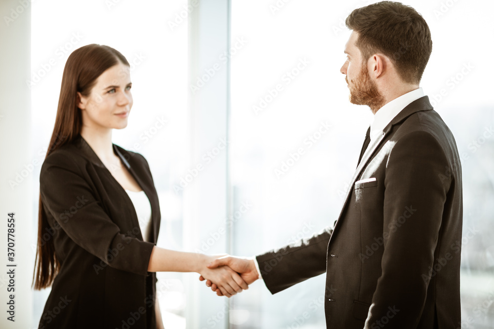 Successful business concept. Young businesswoman and businessman shake hands after signing partnership cooperation contract in office. Two managers man and woman teamwork indoors.