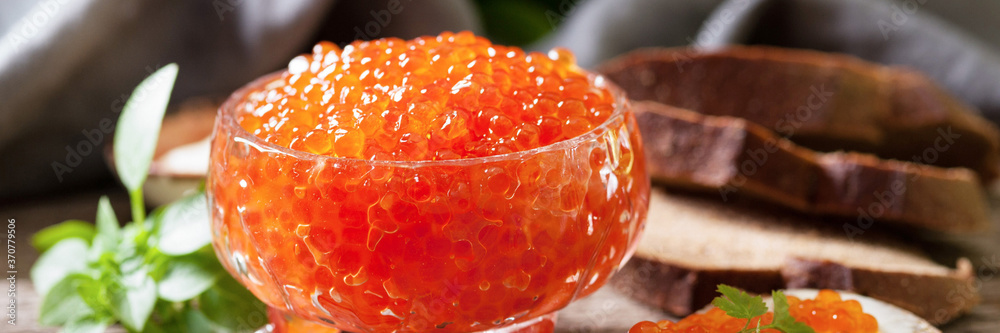 Red caviar close-up. Red caviar in a glass bowl on a wooden table. Banner with space for text	