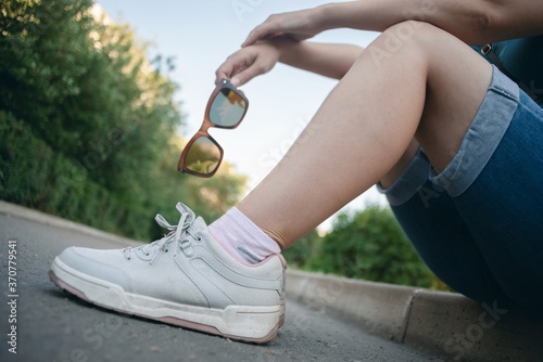 Woman with sunglasses in hands is sitting on the ground.