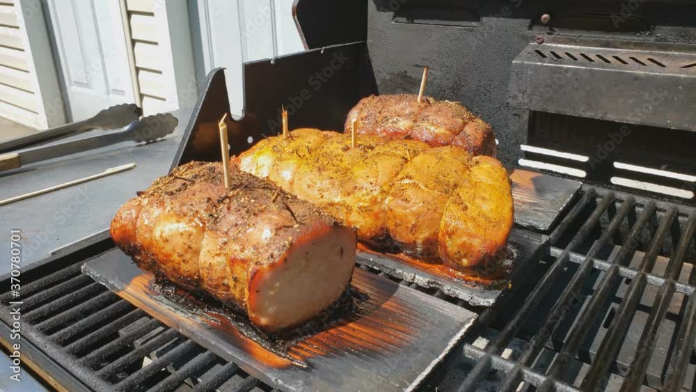 Home cooking - Slowly smoking three half loin pork hams on ceder planks being baked on gas grill. Smoke rise as cedar planks slowly burns.
