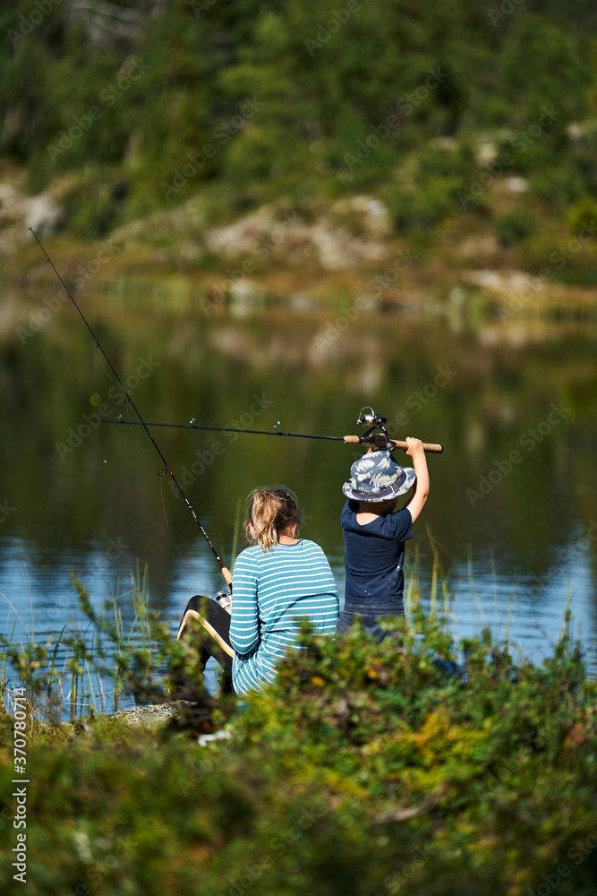 A young girl with her little brother fishes in a small lake. Shot in the deep wild forest of Hallingdal, Gol, Norway. A young girl with her little brother fishes in a small lake. Shot in the deep wild forest of Hallingdal, Gol, Norway.