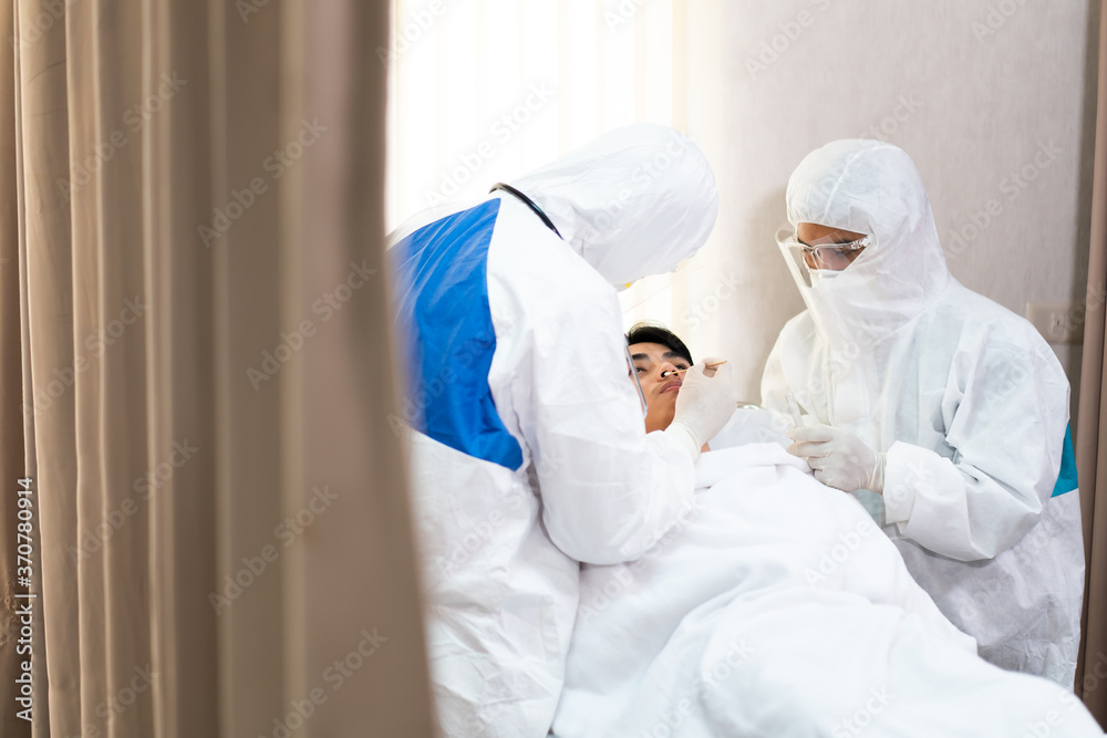 Naklejka premium Two medical technicians wearing full protective equipment collected samples from Asian young man lying in a hospital bed, the operation of the coronavirus mobile testing unit.