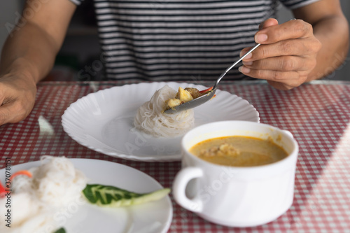 woman use spoon eating green curry with Thai noodle in restaurant