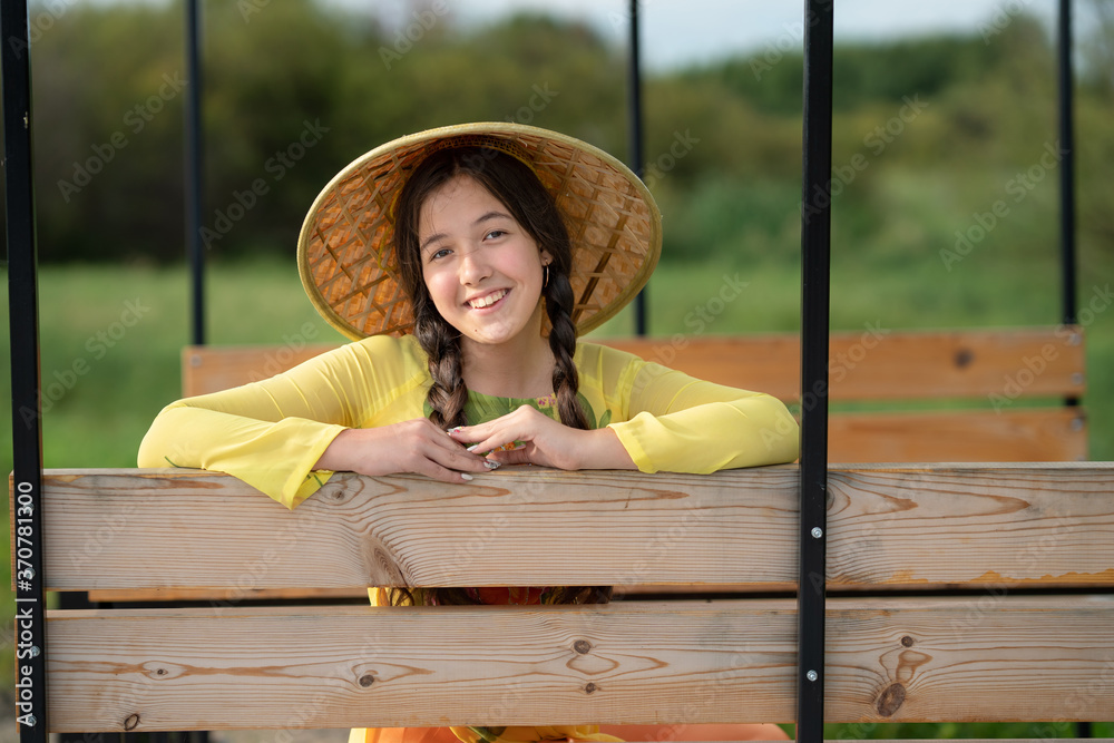 Obraz premium Beautiful teen girl looking at the camera. Happy smiling girl sitting in a wooden carriage of rickshaw and looking at the camera. Asia travel concept. Wooden alcove.
