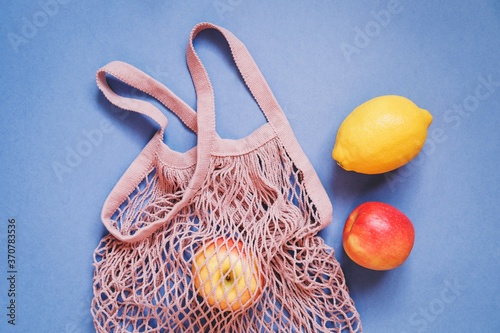 Pink fishnet cotton bag, red apples and lemon on a blue background. Flat lay composition food photography