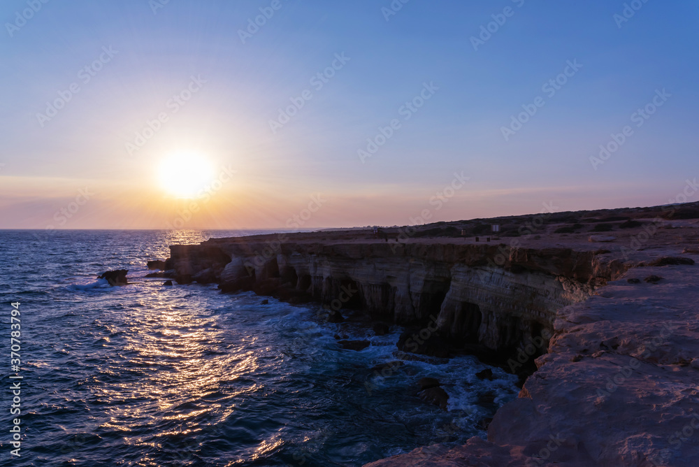 A steep cliff going into the sea against the backdrop of the setting sun