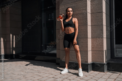 Beautiful woman, summer in city, fitness training on street, posing against window, sportswear. Background glass windows of a building.