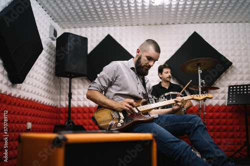 Rock band musicians doing rehearsal before final recording. Rock band playing music instruments while recording in soundproof music studio.