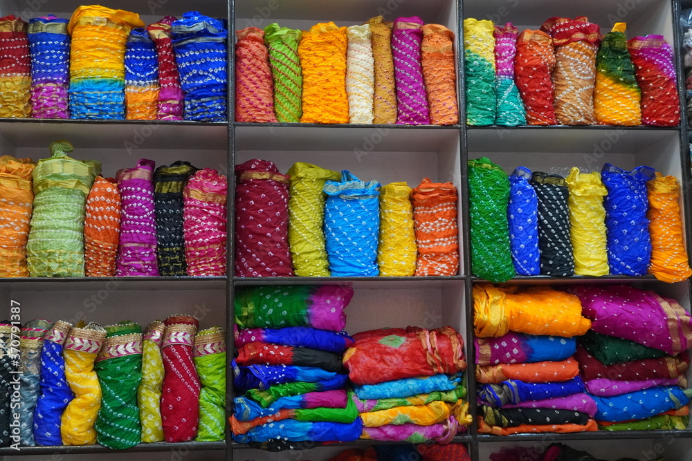 Traditional Rajasthan dress materials is neatly stacked for sale in a cloth merchant shop in India. Colorful fabric street stall. Bandhej or Bandhani widely used in Rajasthan