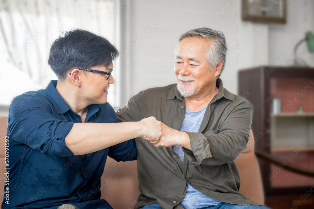 Cheerful senior asian father and middle aged son fists bumping, mature aged dad and millennial man sitting on couch in living room at home, Happiness Asian family concepts Cheerful senior asian father and middle aged son fists bumping, mature aged dad and millennial man sitting on couch in living room at home, Happiness Asian family concepts