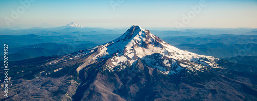 A summer aerial shot of Mt Hood with much of its snow melted and showing layered hills and Mt Jefferson in background