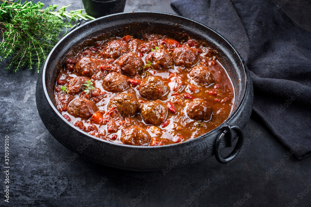 Traditional slow cooked American Tex Mex meatballs chili with mincemeat and beans in a spicy sauce offered as close-up in a design cast-iron roasting dish Traditional slow cooked American Tex Mex meatballs chili with mincemeat and beans in a spicy sauce offered as close-up in a design cast-iron roasting dish