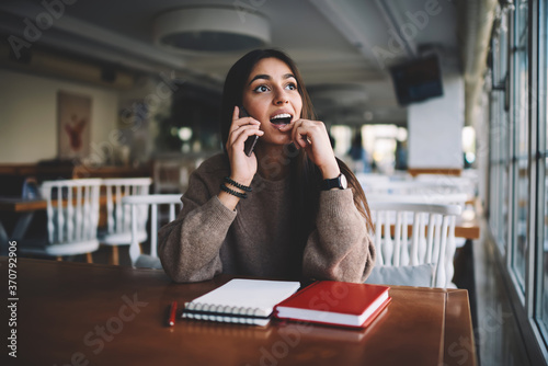 Surprised attractive administrative manager of coffee shop dressed in casual wear worried about confirming money transfer calling to banking service, hipster girl wondering while calling to friend