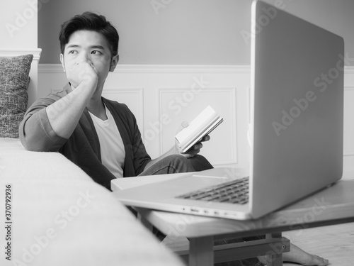 Young asian man reading a book while relaxing at home in black and white photo