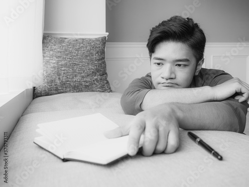 Young asian man taking break after reading book at home in black and white photo