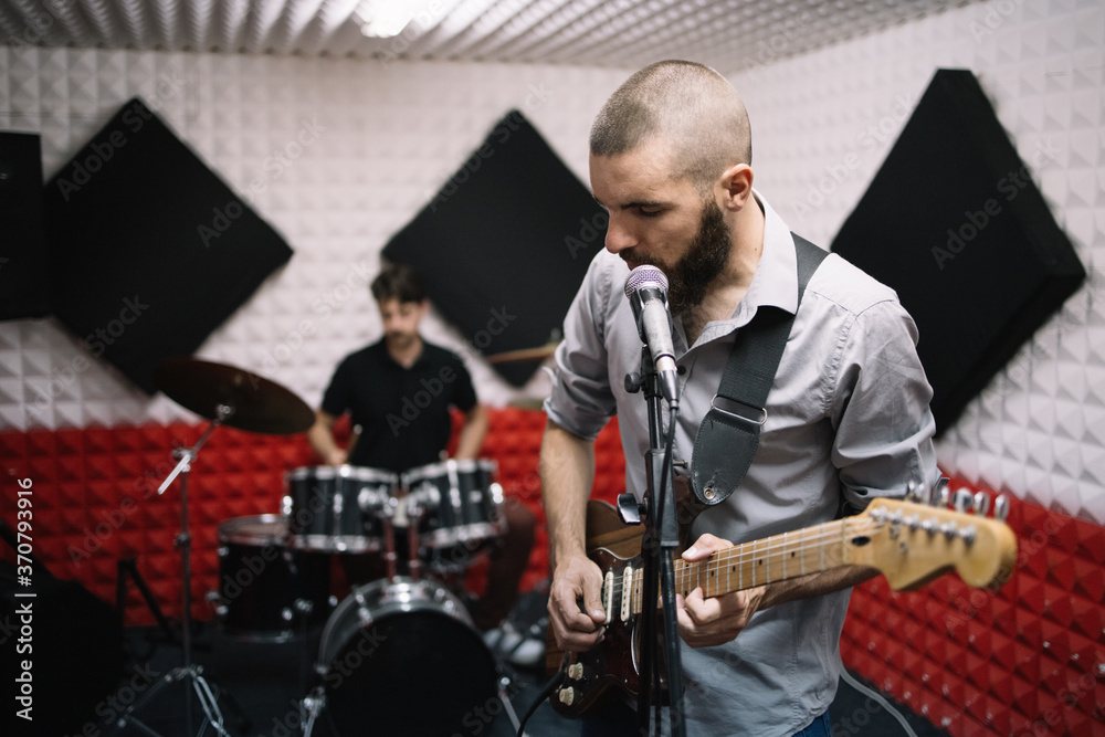 Fototapeta premium Electric guitar player and drummer behind the drum set. Rock band working in music recording studio with sound speakers.