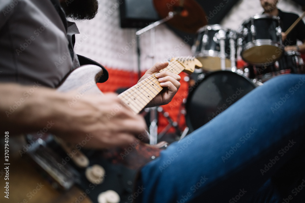 Close-up view of cropped man playing guitar. Cropped guitar player sitting on ground next to blurred drummer. Close-up view of cropped man playing guitar. Cropped guitar player sitting on ground next to blurred drummer.