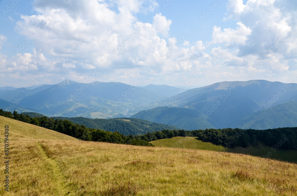 Summer landscape of a forested mountain range and grassy valleys under a cloudy sky. The village of Kolochava and Mount Strymba in the background. Carpathian mountains, Transcarpathia, Ukraine