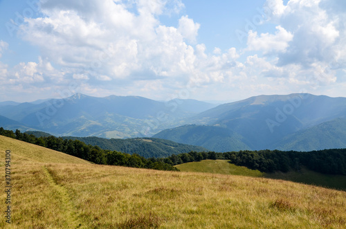 Summer landscape of a forested mountain range and grassy valleys under a cloudy sky. The village of Kolochava and Mount Strymba in the background. Carpathian mountains, Transcarpathia, Ukraine