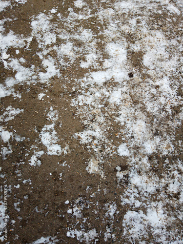The ground, stones and snow of the road in the spring time, look like a background image in close-up. © VLADIMIR